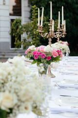 a bouquet of white roses, pink roses, pink carnations on a festive table with dishes decorated with large candelabra on a background of greenery of garden