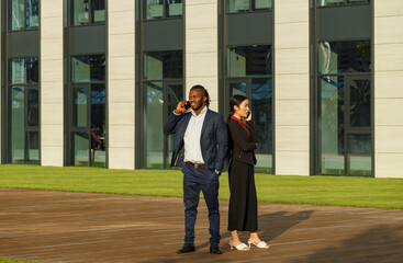 Business partners African American man in navy suit and young Asian brunette long-haired woman solve work issues using phones near office lawn - 471980052