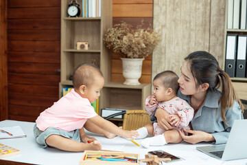 Obraz premium Busy woman trying to work while babysitting two kids. Young Asian mother talking and playing with two children playing around her . Working women with multitasking.