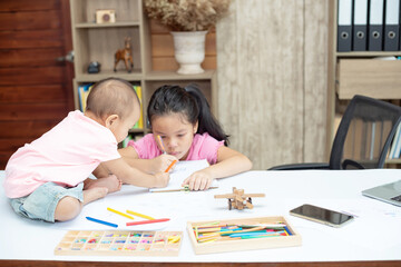 Little toddler girl sit on the working table, her older sister sitting and playing together while mother not home