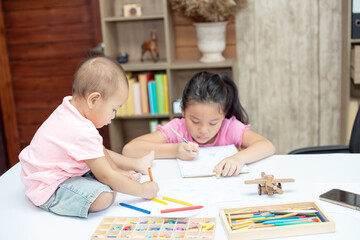 Fototapeta premium Little toddler girl sit on the working table, her older sister sitting and playing together while mother not home
