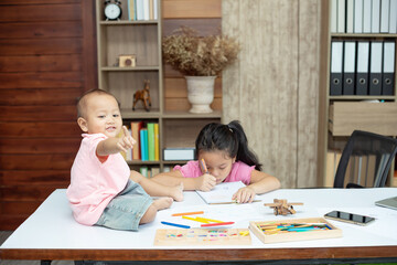 Little toddler girl sit on the working table, her older sister sitting and playing together while mother not home
