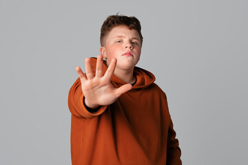 Confident serious teenager boy showing stop sign, lifting open palm and saying No