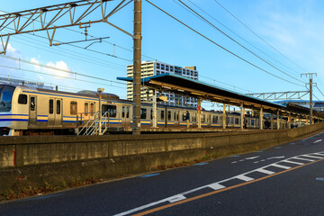 道路に並行した駅に進入する電車とプラットフォームで待つ乗客