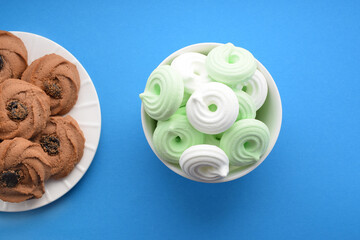 Cookies with jam and multi-colored meringue in white plates on a colored background. Top view, flat lay.
