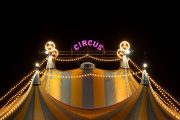 A circus tent at night with its colorful lights on
