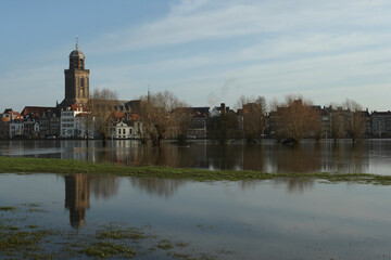 Fototapeta na wymiar A view on the old buildings and the Great Church in the city of Deventer, the Netherlands, with reflection in a flooded meadow 
