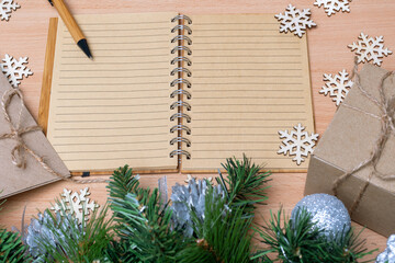 Blank open notebook, diary, pen, gifts in handmade boxes, fir branches and wooden snowflakes. Gift list concept.