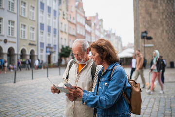 Portrait of senior couple tourists using map and smartphone outdoors in town street