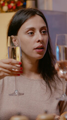 Close up of woman eating food and clinking glass of champagne with husband for christmas eve festivity. Adult enjoying meal and alcohol at festive dinner with man for celebration.