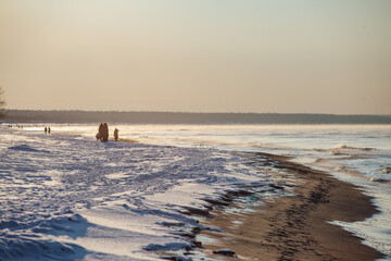 Winter color sunset at sea. A bright color sunset by the sea on a winter day. The beach is snowy. People walk along the sea. The beach is snowy.