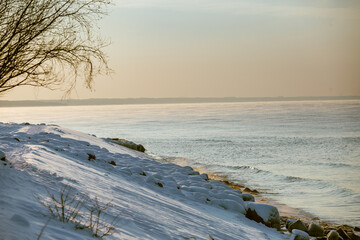 Winter color sunset at sea. A bright color sunset by the sea on a winter day. The beach is snowy. People walk along the sea. The beach is snowy.