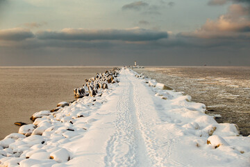 Winter color sunset at sea. A bright color sunset by the sea on a winter day. The beach is snowy. People walk along the sea. The beach is snowy.