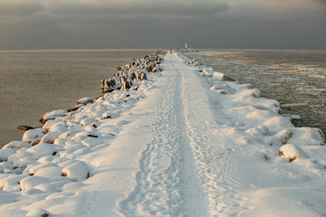 Winter color sunset at sea. A bright color sunset by the sea on a winter day. The beach is snowy. People walk along the sea. The beach is snowy.