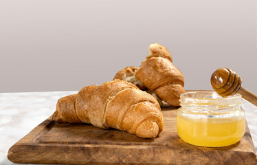 Closeup of jar of sweet honey and croissants on the wooden board against empty background