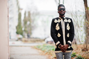 Mega stylish african man in traditional jacket pose. Fashionable black guy in hat and sunglasses.