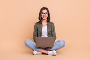 Photo of nice confident smart lady sit floor hold laptop wear glasses khaki shirt jeans isolated beige color background