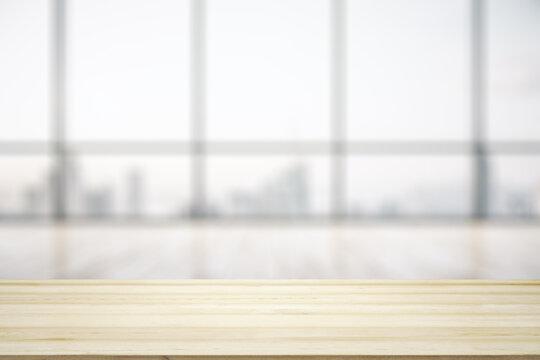 Blank wooden desk with light empty office room with big window on background, mock up