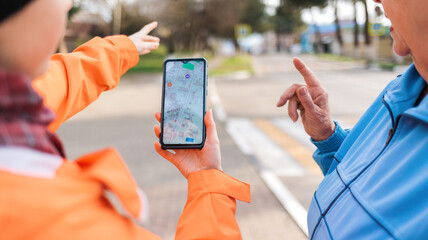 A woman holds a smartphone with an online map and shows the way to an elderly woman with her hand....