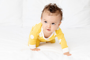Cute baby crawling on white bed looking up