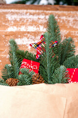 Winter bouquet of fir branches in craft paper, decorated with cones, gift red boxes.The bouquet lies on a wooden bench, covered with snow.Christmas and New Year's concept.Copy space,selective focus.