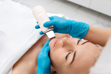 Professional care. A cosmetologist in blue gloves does an ultrasound cleaning chin of a woman's face. Cleansing and rejuvenating procedure in a beauty salon. Top view