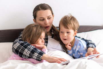 happy family. Close up loving mother lying with daughter son two kids pajamas in bed children reading interesting storybook, preschool smiling kid girl enjoy fairytale before go to sleep good pastime