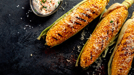 Grilled corncobs with cheese on dark background.