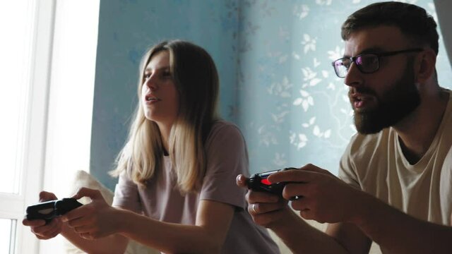 Excited lovely couple playing video games with joystick, happy man and woman playing together, remote video games on a date at home