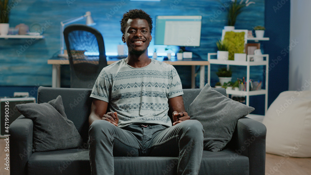 Poster pov of person smiling and sitting on couch. portrait of young adult looking at camera and enjoying f