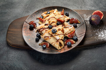 Sweet crepes with figs and chocolate on gray background.