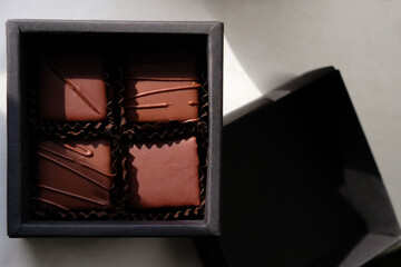 Fototapeta na wymiar Chocolate gift set in a black box. Four pralines in brown paper cups. Craft chocolate in Ukraine. Natural sunlight.