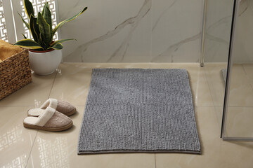 Soft grey bath mat and slippers on floor indoors - obrazy, fototapety, plakaty
