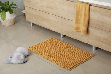 Soft orange bath mat and slippers on floor indoors