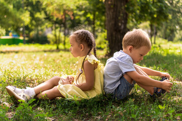 Naklejka na ściany i meble Two happy smiling cheerful toddler preschool twins siblings children brother sister boy girl sitting together on grass lawn in park in sunny hot summer weather. childhood, friendship, family concept