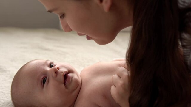 Authentic close up shot young neo mother mum is playing with nake newborn child baby on white soft bed in nursery morning Day. Concept of children, parenthood, childhood, life, maternity, motherhood