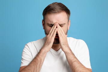 Young man suffering from headache on light blue background