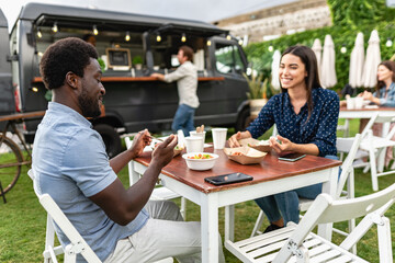 Happy multiracial friends having fun eating in a street food truck market