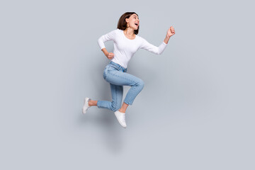 Photo of charming pretty lady dressed white clothes smiling running fast looking empty space jumping high isolated grey color background