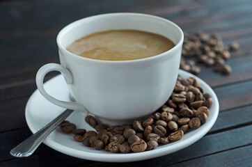 a cup of coffee with cream and coffee beans on a saucer.