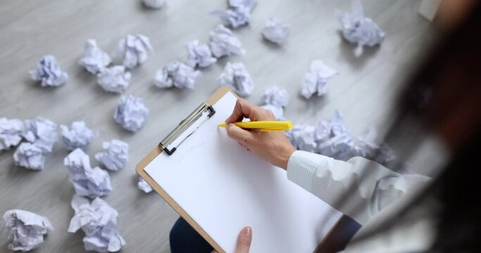 Woman writing business plan near documents crumpled and scattered on floor 4k movie slow motion