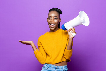 Portrait of smiling African American woman holding megaphone and opening hand in isolated purple studio background - obrazy, fototapety, plakaty