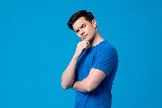 Young curious handsome Caucasian man thinking with hand touching chin in  isolated studio blue background