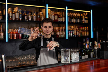 Bartender in apron adds ingredient to glass
