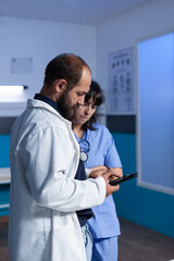 Fototapeta premium Medic and assistant working with digital tablet for healthcare at night shift. Medical nurse and doctor using gadget with touch screen, working late in office. People looking at screen