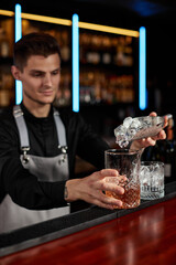 Barman puts the ice cubes into a glass with alcoholic drink