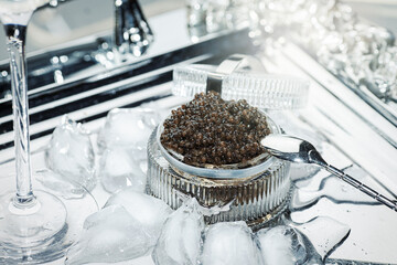 Black caviar. Black sturgeon caviar in a cut-glass bowl and a metal spoon on a silver tray filled with ice.