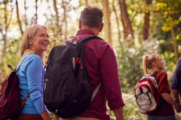 Rear View Of Mature And Mid Adult Couples In Countryside Hiking Along Path Through Forest Together