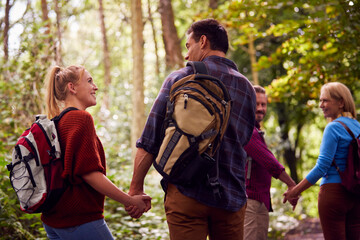 Rear View Of Mature And Mid Adult Couples In Countryside Hiking Along Path Through Forest Together