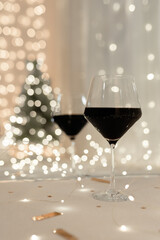 A glass of wine. Reflection of a glass and new flowers of the Christmas tree of lights in the mirror. Blurred lights